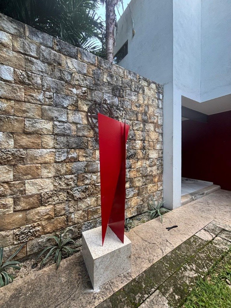 Escultura tridimensional en acero con acabado rojo carmín sobre cantera